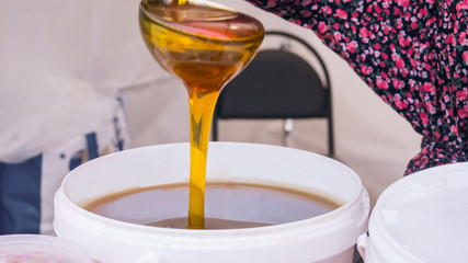 Woman pouring sweet honey from the ladle at outdoor market