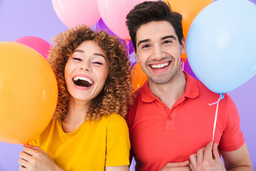 Image of happy couple man and woman smiling at camera while standing with multicolored air balloons