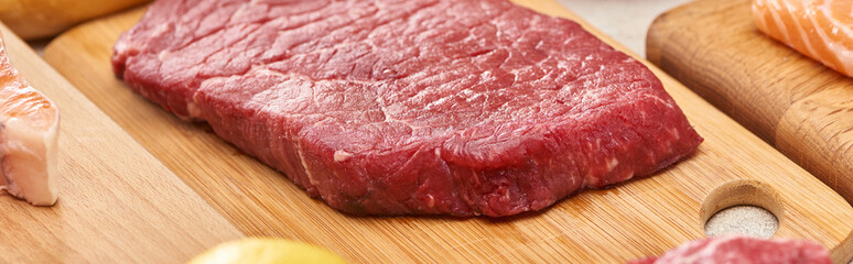 Panoramic shot of raw meat steak on wooden cutting board