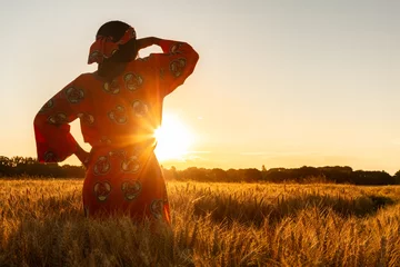 Foto op Canvas African woman in traditional clothes standing in a field of crops at sunset or sunrise © Darren Baker