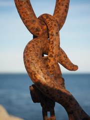 An old rusty hook and shackle on a crane, with blue sky behind.