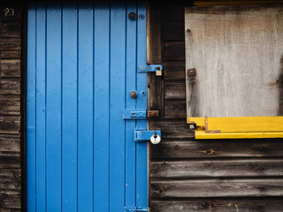 Blue door on a bleached black wooden shed with a yellow window sill