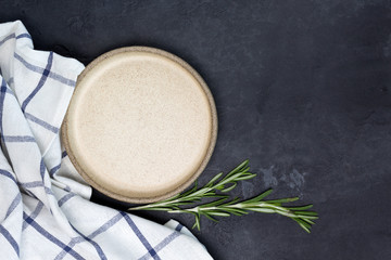 Round beige clay plate, towel, rosemary, pepper on dark concrete background. Cooking, recipe concept. Top view, flat lay, mock up, copy space