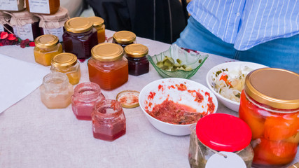 Jars with homemade fruit jams and pickled tomatos at outdoor market, home-cooked food, gastronomy and streetfood festival concept