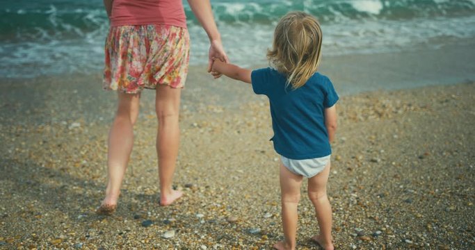 Young mother on beach offering toddler her hand