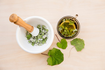 Dried Tussilago farfara( coughwort, tash plant, farfara) commonly known as coltsfoot believed to be natural cough remedy. Tea glass with fresh leaves, herbal medicine concept on wooden background.