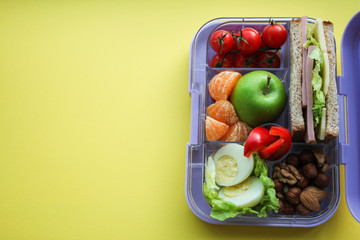 Lilac lunch box with useful food for lunch and snack: sandwich, vegetables, fruits, nuts and eggs...