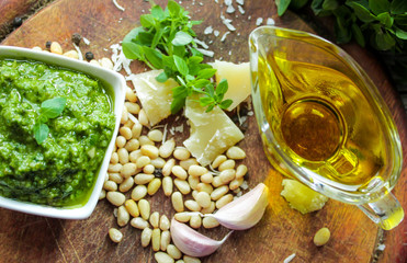 A bowl with pesto sauce and ingredients for its preparation: green Basil, Parmesan cheese, olive oil, pine nuts, salt and garlic on the background of aged boards