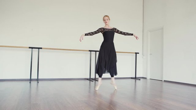 Professional ballerina in pointe shoes rehearsing dance in ballet studio. Female ballet dancer wearing black lace leotard and long wrap skirt in practice