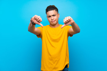 Young man with yellow shirt over isolated blue background showing thumb down