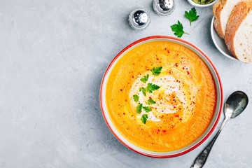 Carrot and pumpkin cream soup with parsley on gray stone background.