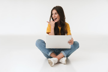 Surprised young woman isolated over white wall background using laptop computer pointing.