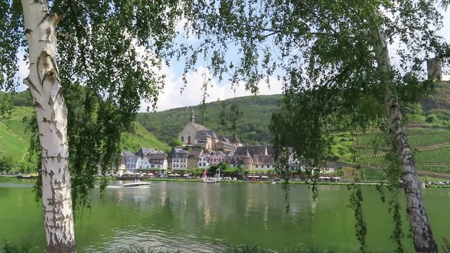 cityscape of Beilstein at Moselle River with motorboat passing by on river.