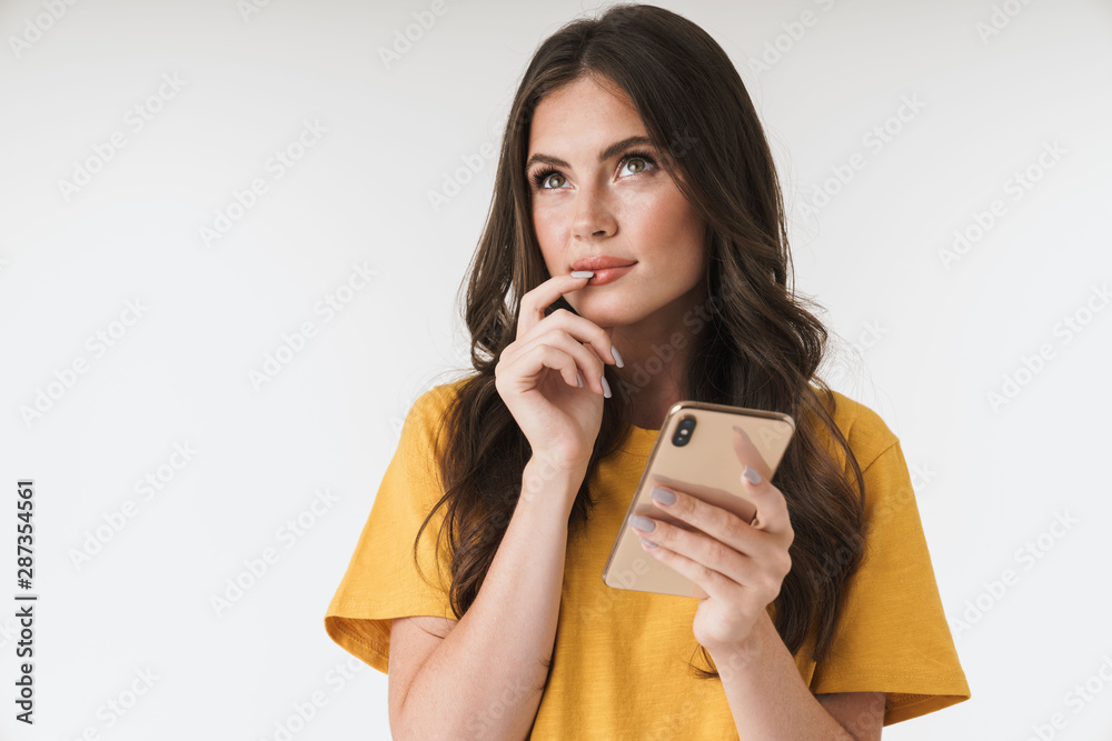 Sticker Thoughtful young woman posing isolated over white wall background using mobile phone.