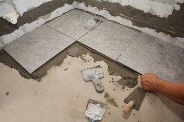 Builder installing ceramic tile on the floor, bathroom flooring. Floor tiling