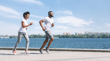 Afro man and woman jogging outdoor along river bank