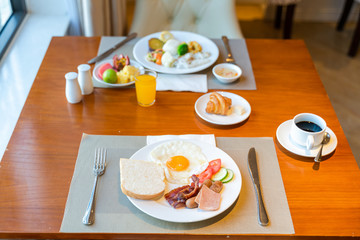 Fresh breakfast table next to window with bread, pastry, egg, fruit, juice, coffee cup