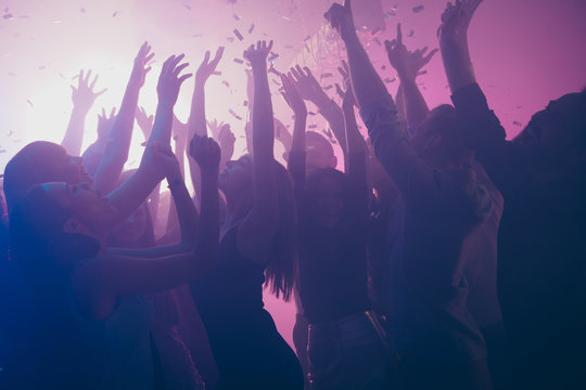 Close up photo of many festive excited people dancing clubbing purple lights confetti fog nightclub hands raised shiny formal-wear