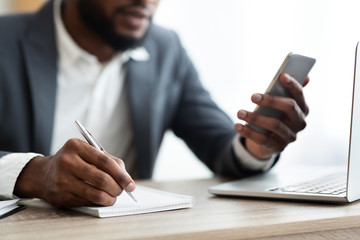 African American employer using smartphone and taking notes in office