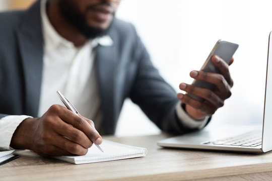 African American employer using smartphone and taking notes in office