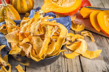 Sun-dried organic pumpkin slices, hokkaido butternut squash chips, on old rustic wooden background with fresh sliced pumpkin
