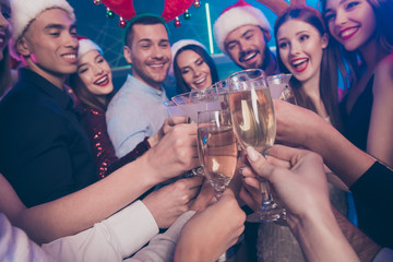 Close-up view of nice attractive glamorous cheerful cheery positive girls and guys having fun clinking wineglass greetings December winter tradition in luxury place nightclub lights indoors
