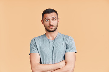 Surprised and shocked young man with crossed arms looking to camera over beige background