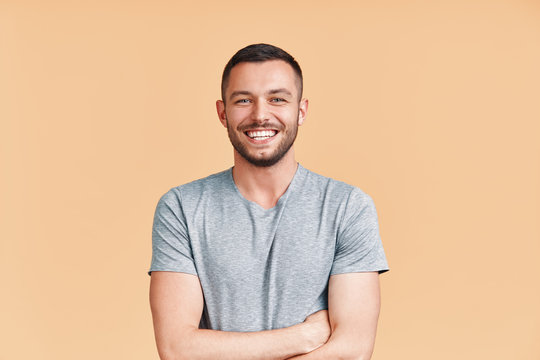 Happy smiling handsome man with crossed arms looking to camera over beige background