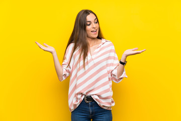 Young woman over isolated yellow background holding copyspace with two hands