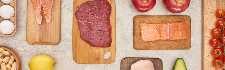 Panoramic shot of wooden cutting boards with meat and fish near vegetables on marble surface