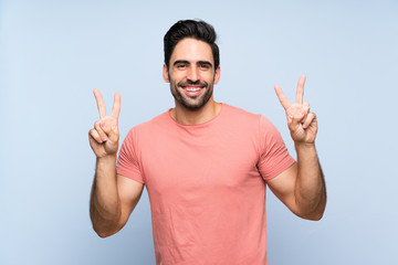 Handsome young man in pink shirt over isolated blue background showing victory sign with both hands