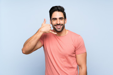 Fototapeta premium Handsome young man in pink shirt over isolated blue background making phone gesture. Call me back sign