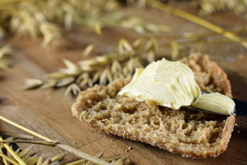 Oat bread with margarine. Oat ears of grain on brown wooden table.