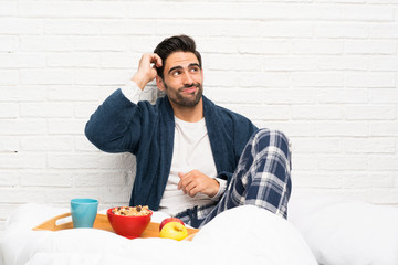 Man in bed with dressing gown and having breakfast having doubts and with confuse face expression