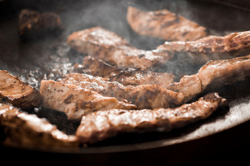 Close up of grilled meat on grid on black background with steam