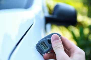 Male hand holds device for measuring coating thickness before polishing car.  Measuring thickness of the car paint coating with paint thickness gauge. Polish car concept