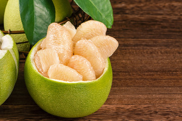 Fresh peeled pomelo, grapefruit, shaddock with green leaves on dark wooden plank table. Seasonal fruit near mid-autumn festival, close up, copy space