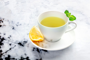 A cup of tea with a slice of lemon and mint leaves, with an organic shadow and copy space