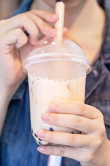 Young girl in denim jacket is drinking brown sugar flavored tapioca pearl bubble milk tea with glass straw in night market of Taiwan, close up, bokeh