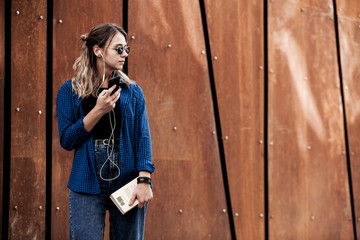 Portrait of a happy girl listening music on line with headphones from a smartphone in the street in a summer sunny day. Woman listening to music with the phone and having fun