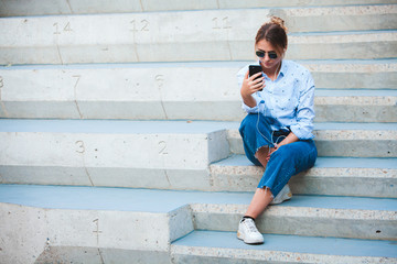 Portrait of a happy girl listening music on line with headphones from a smartphone in the street in a summer sunny day. Woman listening to music with the phone and having fun