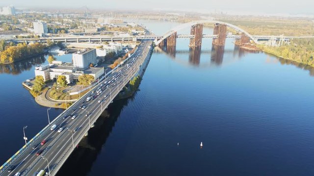 Aerial drone view of Podolskiy bridge construction site and Rybalskiy island with highway road during rush hour traffic jam on bright sunny day in Kiev center, Ukraine.