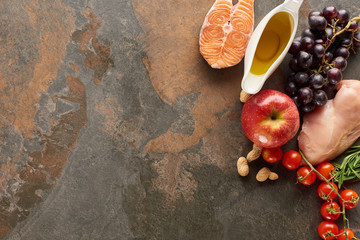 Top view of raw fish and poultry near vegetables, fruits, peanuts and olive oil on marble surface...