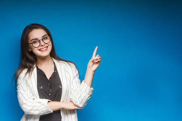 Pretty girl, teacher in eyeglasses show something isolated on blue background. Copy space. Place...