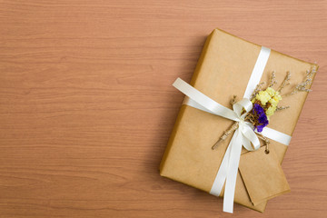 Above brown gift box white ribbon and vintage flowers with tag on wood background with copy space.
