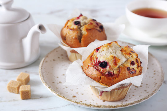Two blueberry muffins, cup of tea and teapot for sweet breakfast