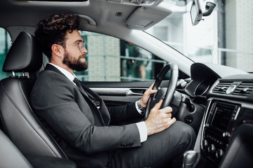 Handsome young bearded driver in full suit driving a car.