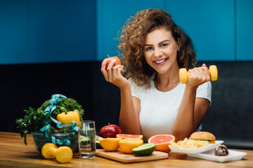 Half body portrait of young healthy  woman holding dumbbell and fresh fruits on hands able to use for diet, healthy, sport, food, or exercise concept.