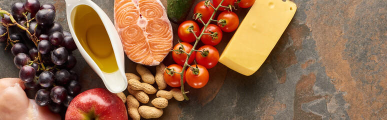 Panoramic shot of raw salmon steak near grape, tomatoes, peanuts, apple, olive oil and cheese on...