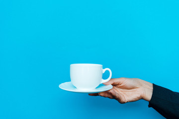 cropped view of woman holding saucer and cup on blue